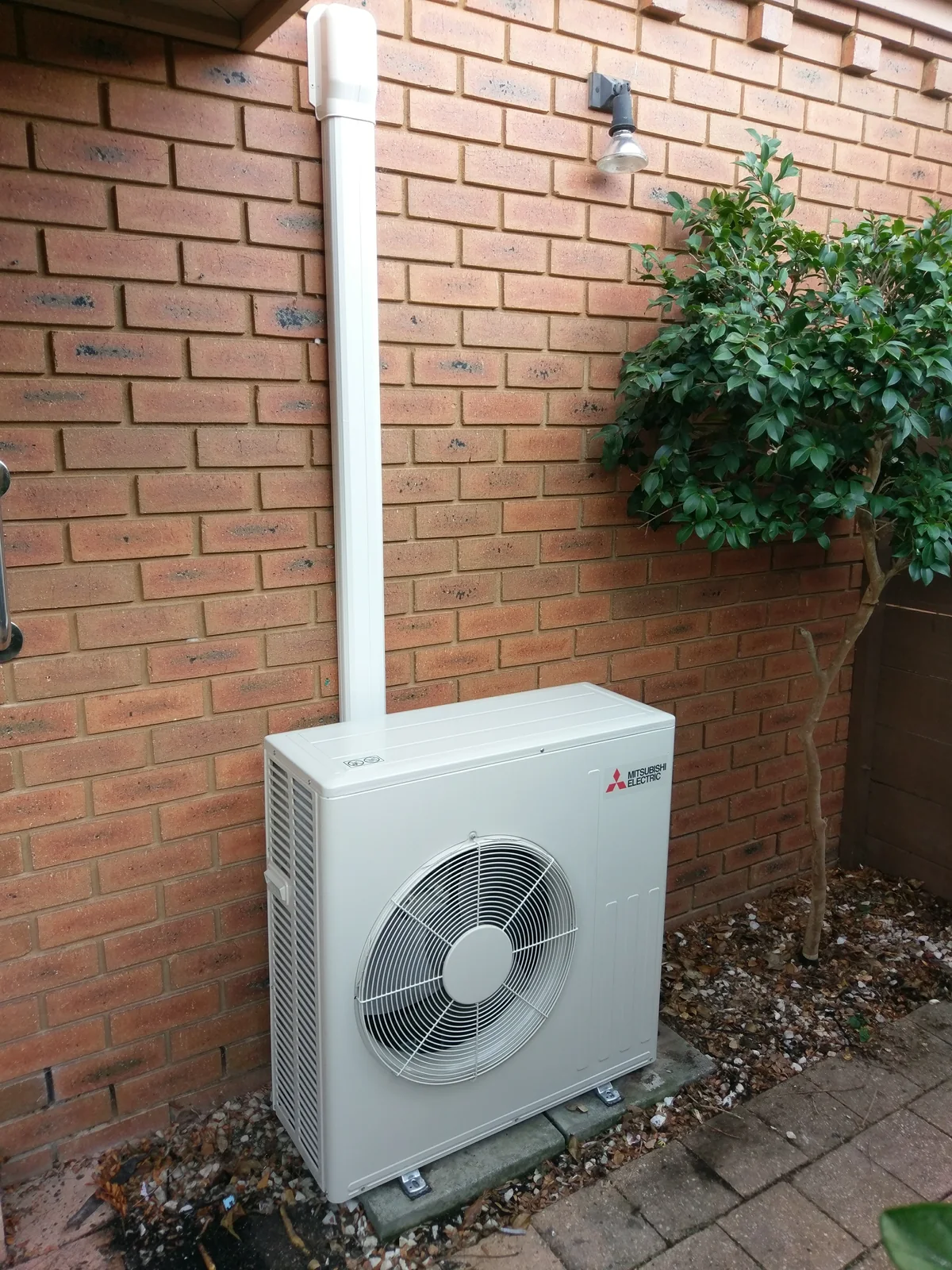 Mitsubishi Electric outdoor unit installed on a brick wall beside a garden bed