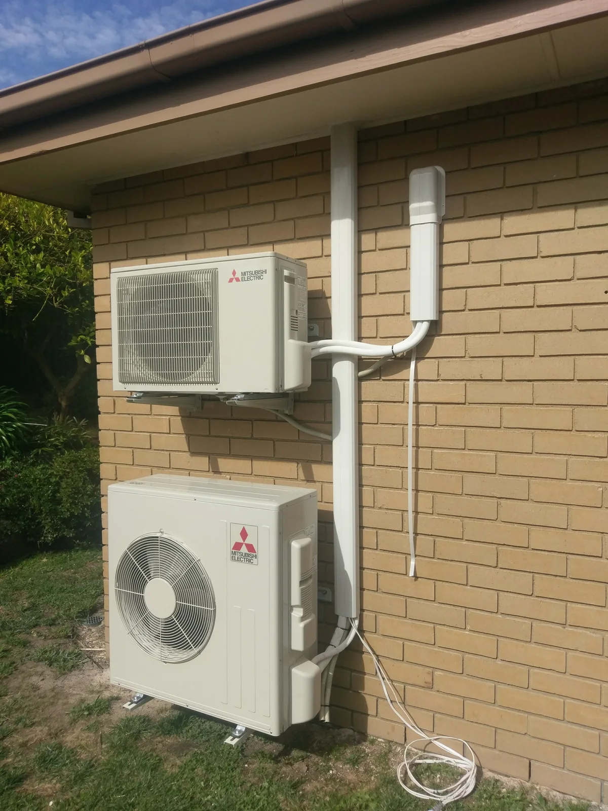 Two Mitsubishi Electric outdoor units stacked on a wall bracket