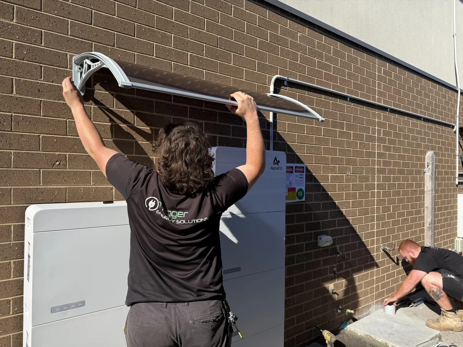 Trigger crew fitting a weather canopy above a home battery