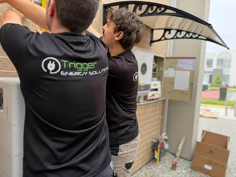 Trigger Energy Solutions technicians fitting a weather awning above a home battery