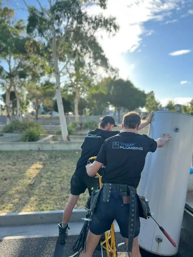 Two Trigger Group technicians carrying a hot water unit