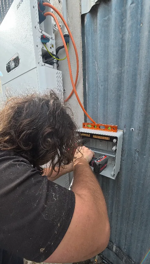 Trigger Energy Solutions electrician levelling a sub board beside a Sofar battery