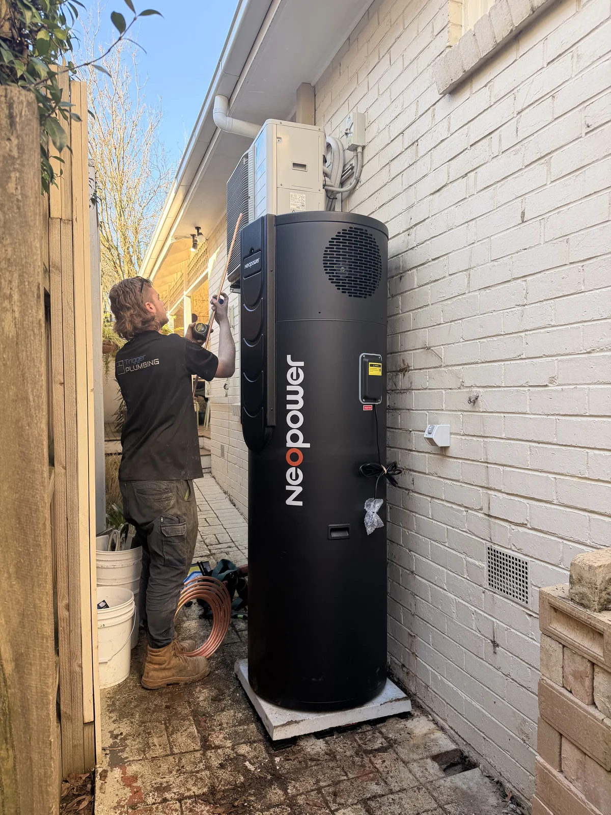 Trigger Plumbing installer commissioning a NeoPower heat pump hot water system down the side of a Melbourne home