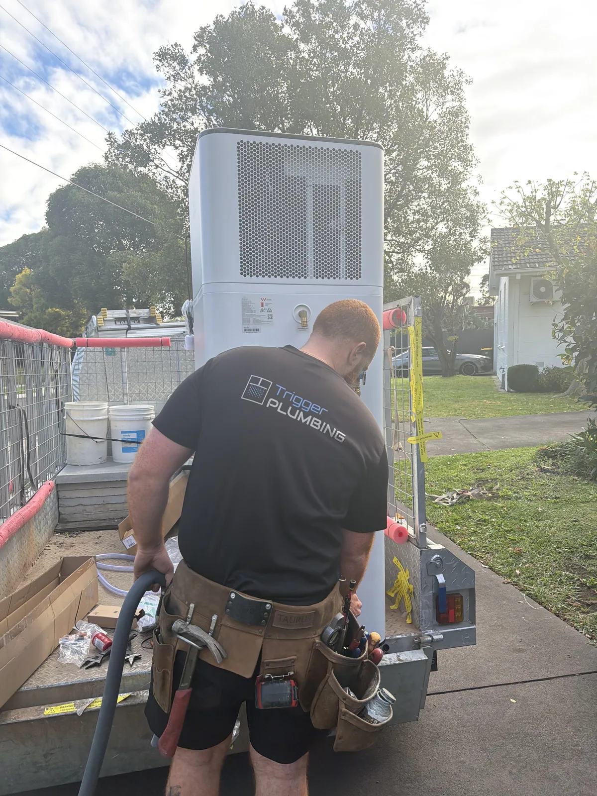 Trigger Plumbing tradesman unloading a heat pump from a trailer